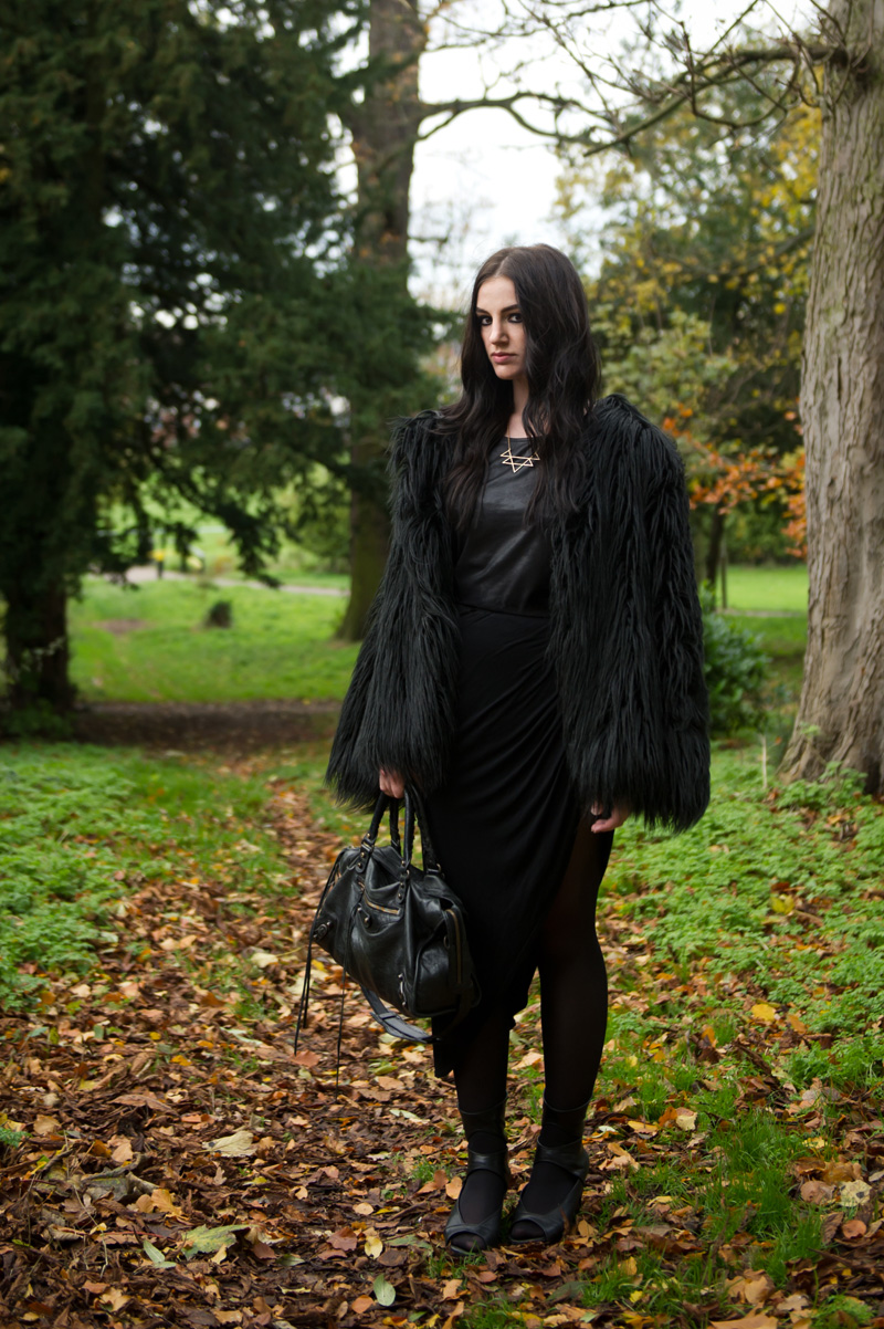 Fashion blogger Stephanie of FAIIINT wearing Lookbook Store faux fur black longhaired coat, H&M leather look tee, RockLove sacred geometry geo necklace, River Island asymmetric skirt, Rick Owens wedges, Balenciaga city bag. All black outfit, Game of Thrones crow coat