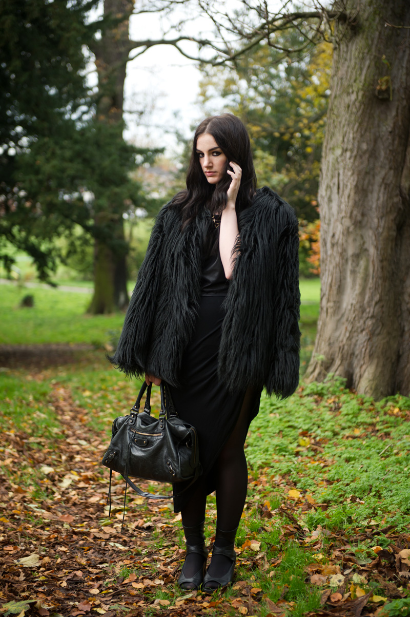 Fashion blogger Stephanie of FAIIINT wearing Lookbook Store faux fur black longhaired coat, H&M leather look tee, RockLove sacred geometry geo necklace, River Island asymmetric skirt, Rick Owens wedges, Balenciaga city bag. All black outfit, Game of Thrones crow coat