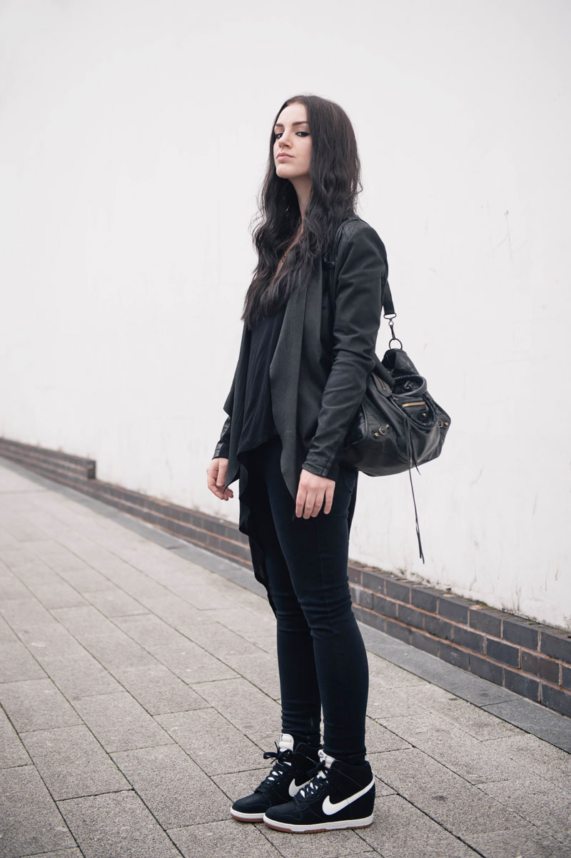 Fashion blogger Stephanie of FAIIINT wearing Barneys Originals draped leather jacket, Topshop skinny jeans & asymmetric top, Nike Sky Hi High Dunk sneakers in black & white, Balenciaga city bag. Casual all black street style outfit.