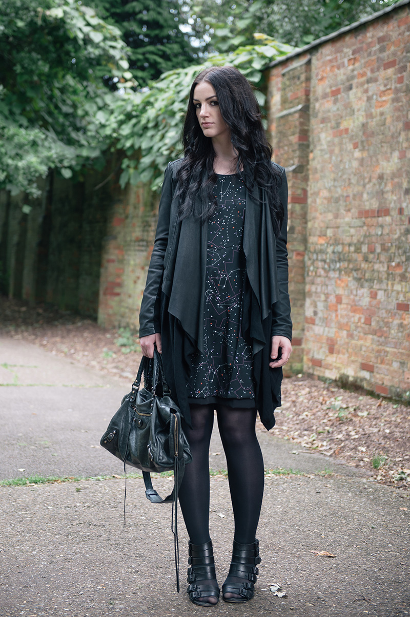 Fashion blogger Stephanie of FAIIINT wearing Barneys Originals draped leather jacket, ASOS cardigan, Yumi constellation print dress, Kurt Geiger buckle wedges, Balenciaga city bag. All black street style outfit.