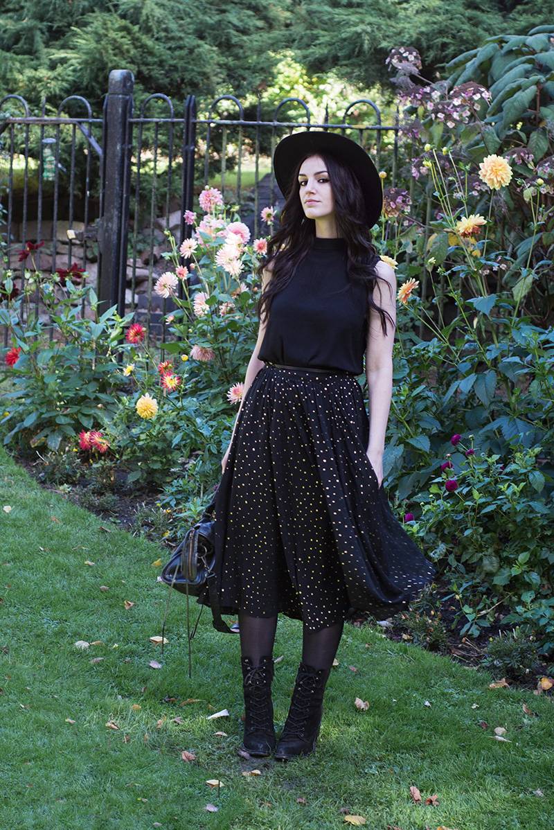 Fashion blogger Stephanie of FAIIINT wearing Catarzi fedora, Yumi button back sleeveless top, Yumi gold spot polka dot pleated chiffon midi skirt, Kurt Geiger 'Saturn' lace up boots and Balenciaga city bag. All black everything, dark street style outfit.