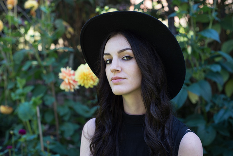 Fashion blogger Stephanie of FAIIINT wearing Catarzi fedora & Yumi sleeveless blouse. Portrait in front of Autumn flowers.