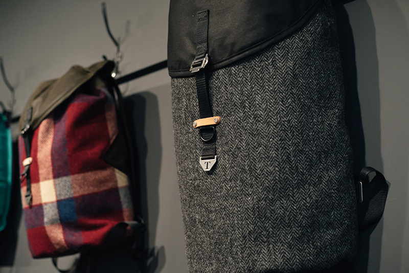 FAIIINT Trakke Glasgow studio. Krukke backpack bag in grey herringbone Harris Tweed and red check.