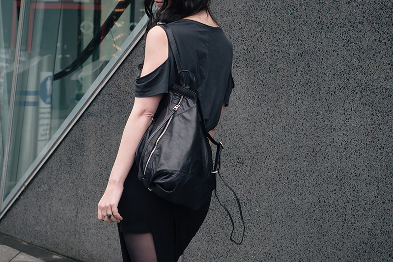 Fashion blogger Stephanie of FAIIINT wearing H&M cold shoulder tee, draped asymmetric skirt, Topshop leather backpack. All black everything street style outfit details.