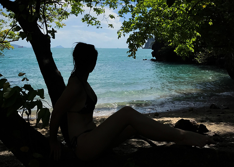 Fashion travel blogger Stephanie of FAIIINT laying in tree silhouette looking over beach and crystal clear blue ocean at Lading Island Hong Islands Thailand.