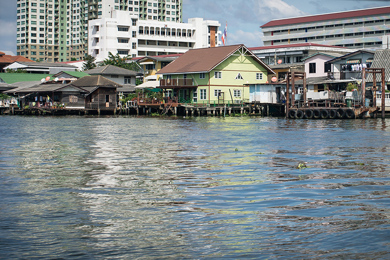 Bangkok Thailand Chao Phraya River ferry, brightly coloured wooden riverside homes on the water.