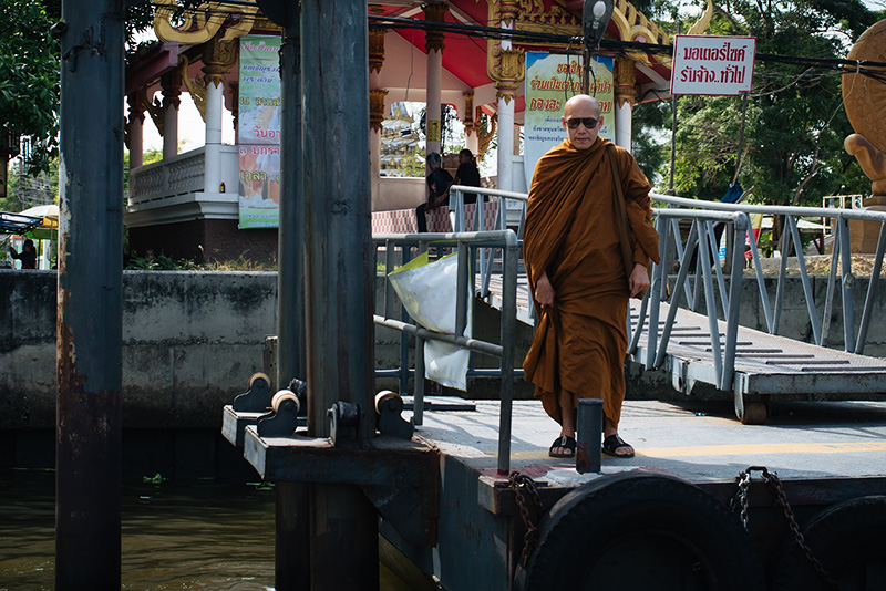 Bangkok Thailand Buddhist monk in sunglasses standing on the dock on the Chao Phraya River.