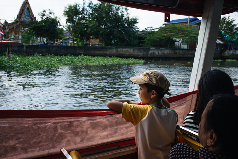 Bangkok Thailand little boy looking out onto the Chao Phraya River from the ferry boat.
