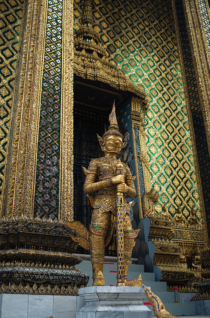 Temples of Bangkok Thailand, The Grand Palace and Wat Phra Kaew, glittering gold mosaic tiles and gold yaksha demon statue guardian at the entrance to Phra Mondop.