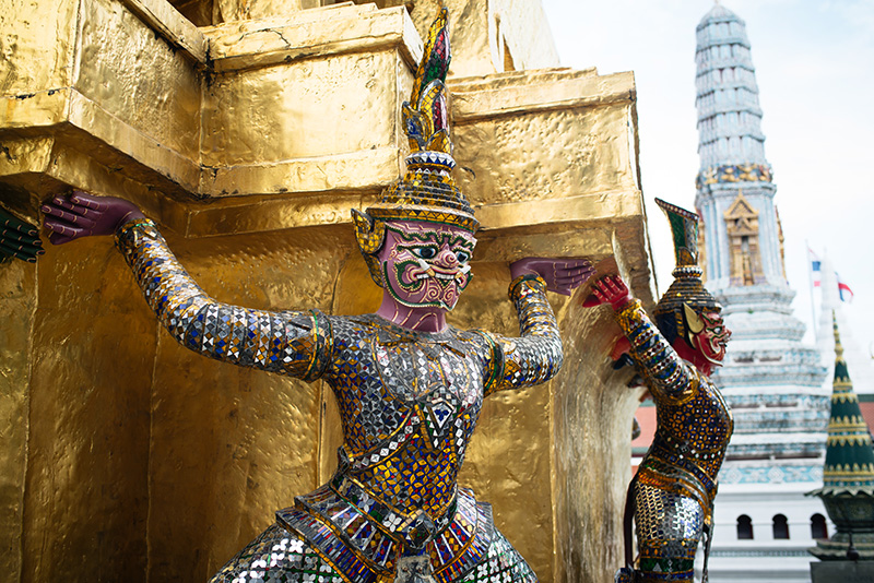 Temples of Bangkok Thailand, The Grand Palace and Wat Phra Kaew, colourful yaksha demon statues around gold stupa.