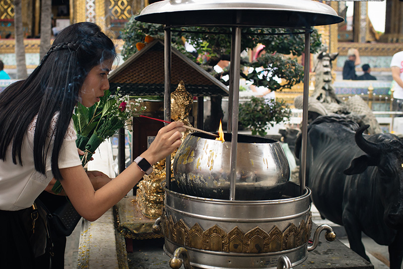 Temples of Bangkok Thailand, The Grand Palace and Wat Phra Kaew, girl lighting incence offering with flowers.