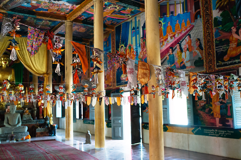 Colourful flags and decorations hanging inside bright painted Buddhist temple in Siem Reap Cambodia.