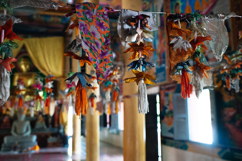 Colourful flags and decorations hanging inside bright painted Buddhist temple in Siem Reap Cambodia.